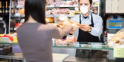 A clerk wearing a black apron and a face mask on handing an item to a woman in a shop.