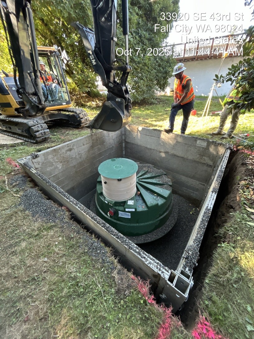 3 workers are installing a septic tank in a large hole in the ground in Fall City.