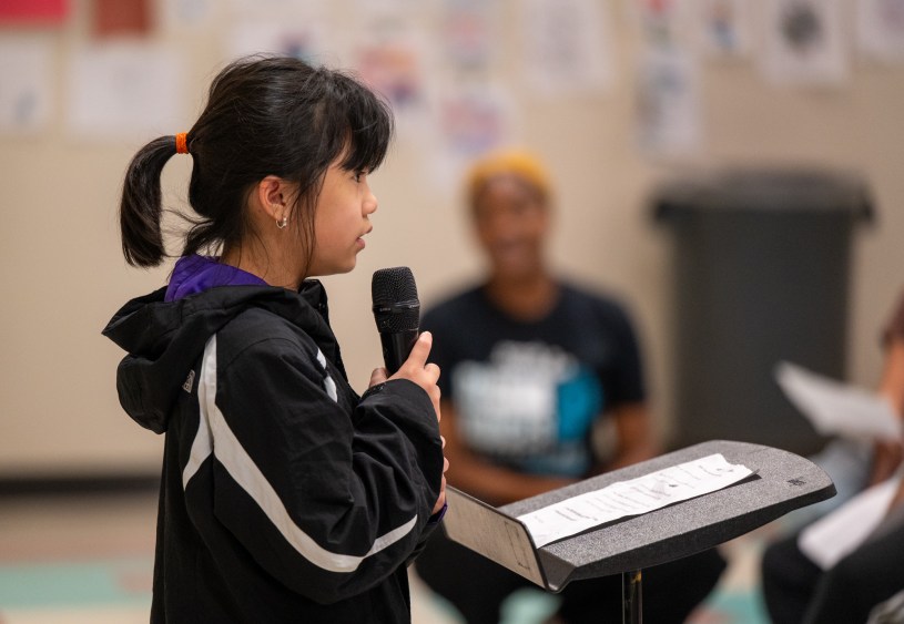 Girl speaks into microphone in front of crowd.