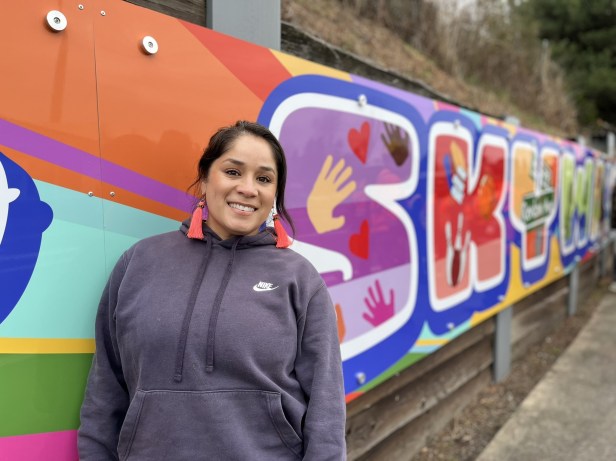Woman stands next to mural that reads welcome to Skyway