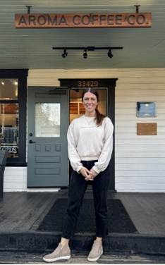 Woman stands in front of her business' sign that reads "Aroma Coffee Co."