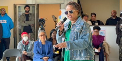 Woman speaking into a microphone in front of a crowd.