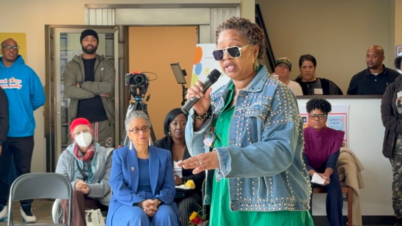 Woman speaking into a microphone in front of a crowd.