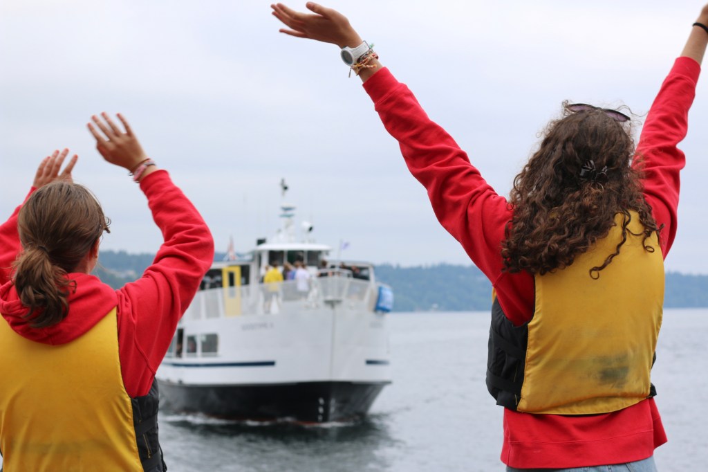 Girls raise their arms in front of a boat in the water