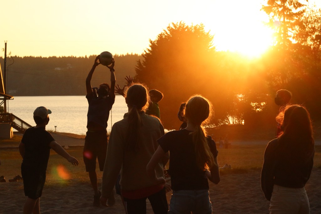 Children playing with a round ball near a beach as the sun sets.