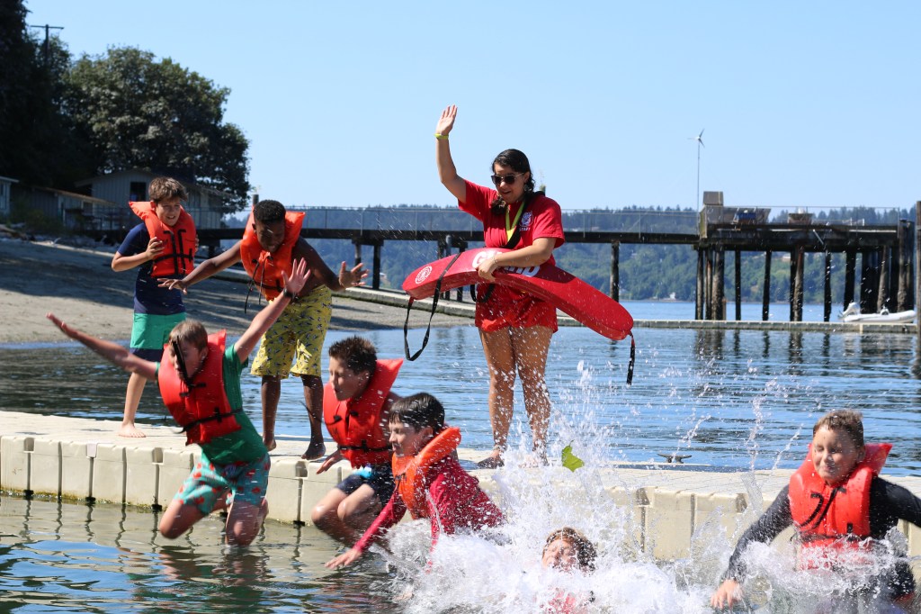 Children playing in the water at a beach with a lifeguard nearby.