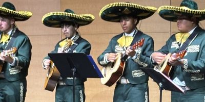 A group of mariachi-style singers on a stage playing instruments