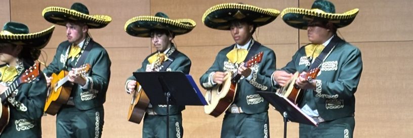 A group of mariachi-style singers on a stage playing instruments
