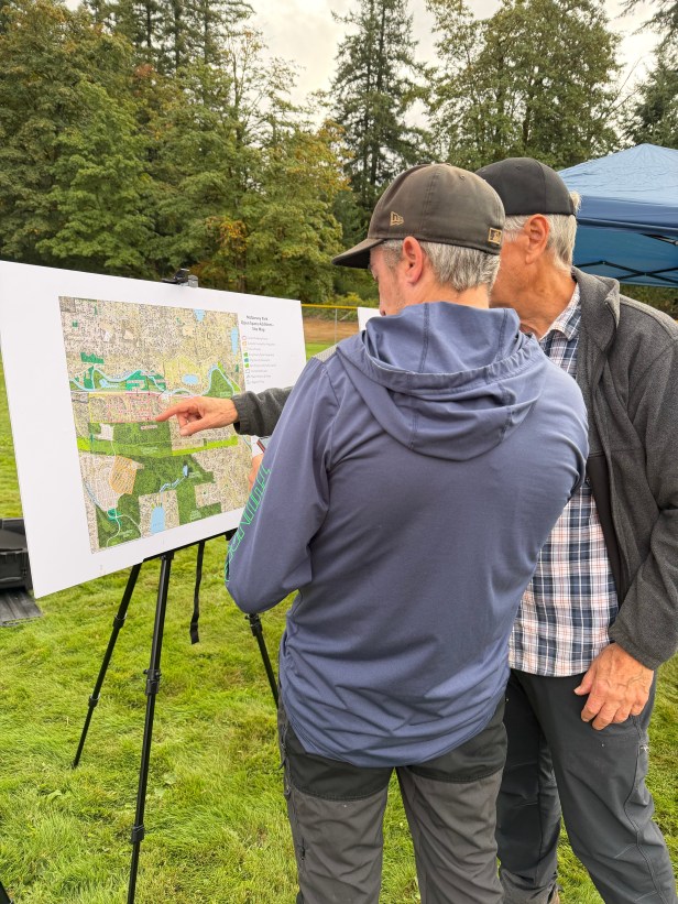 Two people look at a posterboard-sized map at Fairwood's 60th Anniversary Celebration. They are standing on open grass and in the background are trees.