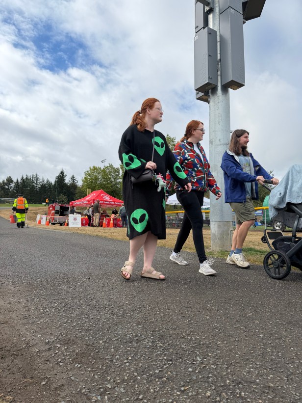 A trio of adults walk along a paved area at Fairwood's 60th Anniversary Celebration on Saturday, Aug. 29, 2026. One of them is pushing a stroller. In the background are vendor booths, tree, and blue sky with clouds.