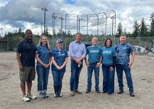 A group of adults pose for a picture at Fairwood's 60th Anniversary Celebration on Saturday, Aug. 29, 2026. They are standing in the infield of a softball field, and behind them is the field's backstop, along with trees and lights.