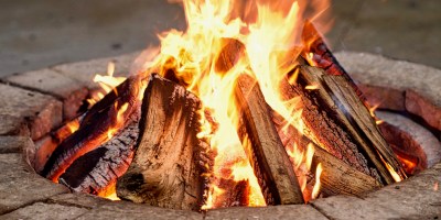 A pile of purposefully stacked wood burns with orange flames inside of a firepit.