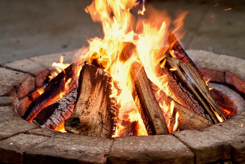 A pile of purposefully stacked wood burns with orange flames inside of a firepit.