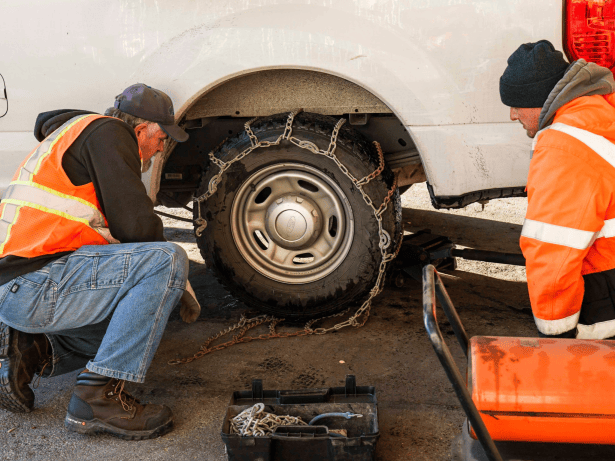 Two men put on chains on a tire of a large vehicle.